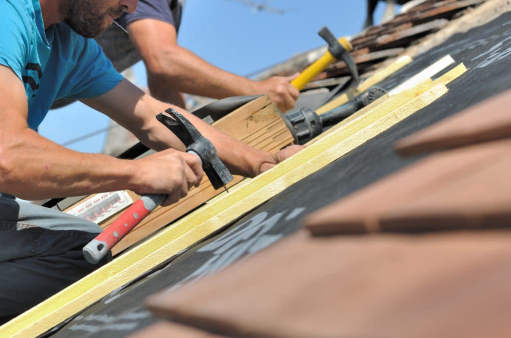 roofer with roofing materials on roof featuring hammer and nails