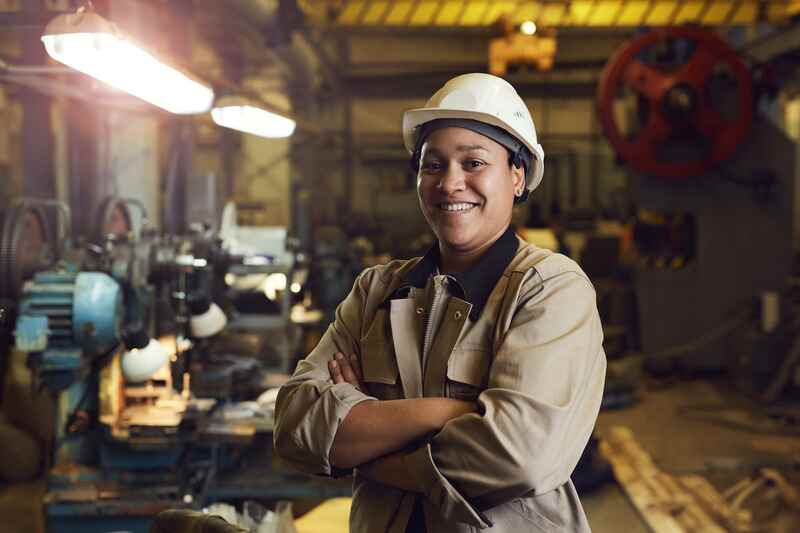 Waist up portrait of mixed-race female worker posing confidently while standing with arms crossed in factory workshop
