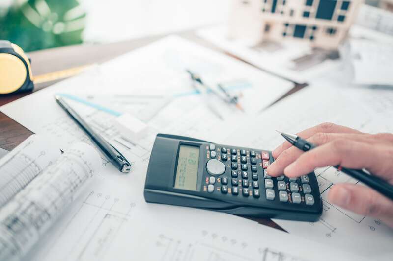 hand with pen and calculator on desk with sheets and papers