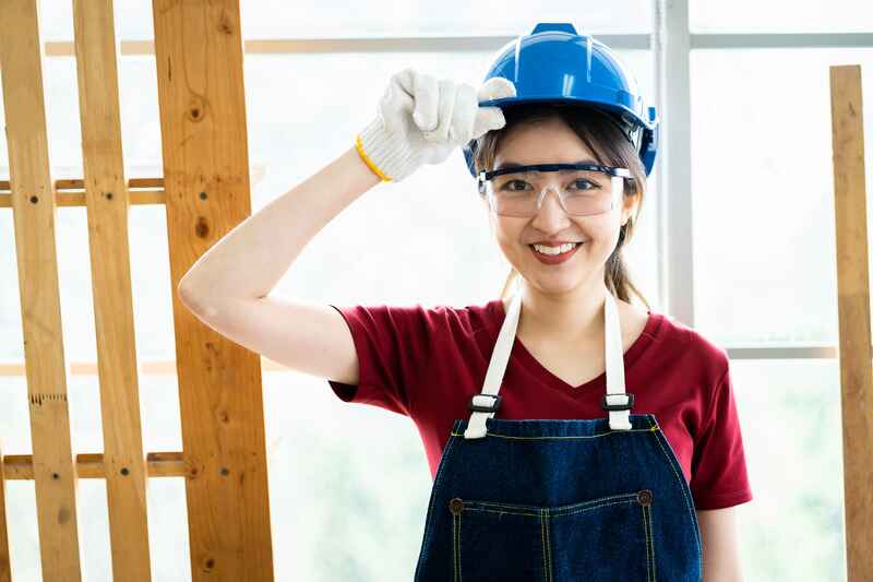 Happy young female carpenter in safety uniform at wood workshop