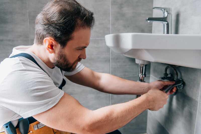Male plumber in working overall fixing sink in bathroom