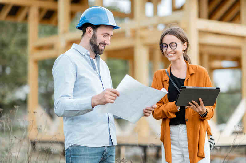 Builder with a female client near the wooden house structure on the construction site