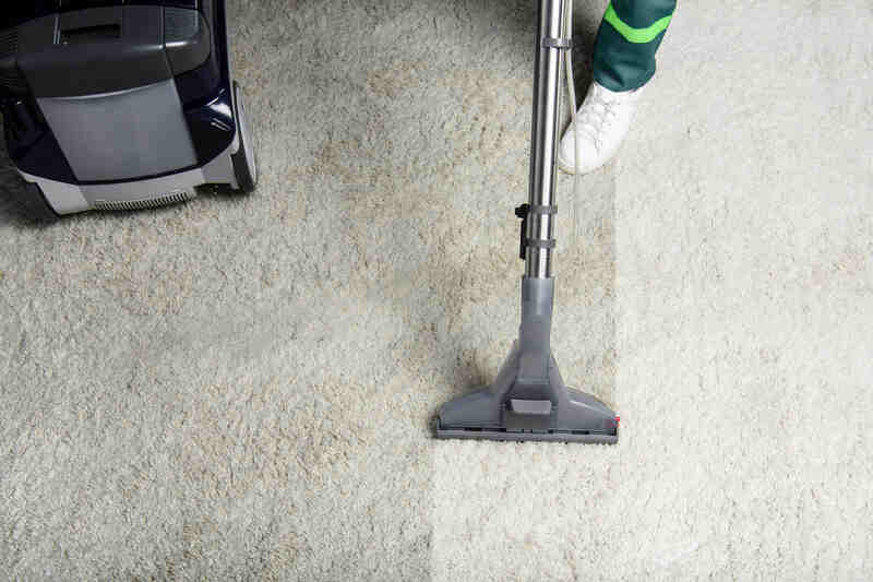 High angle view of person cleaning white carpet with professional carpet cleaner