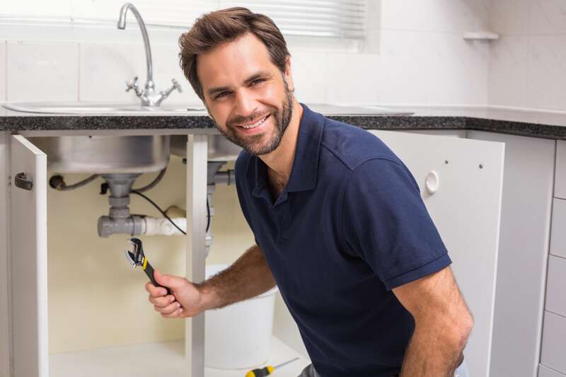 Plumber fixing under the sink smiling at the camera