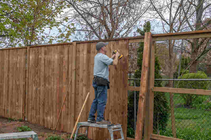 man builds a wooden fence in a back yard