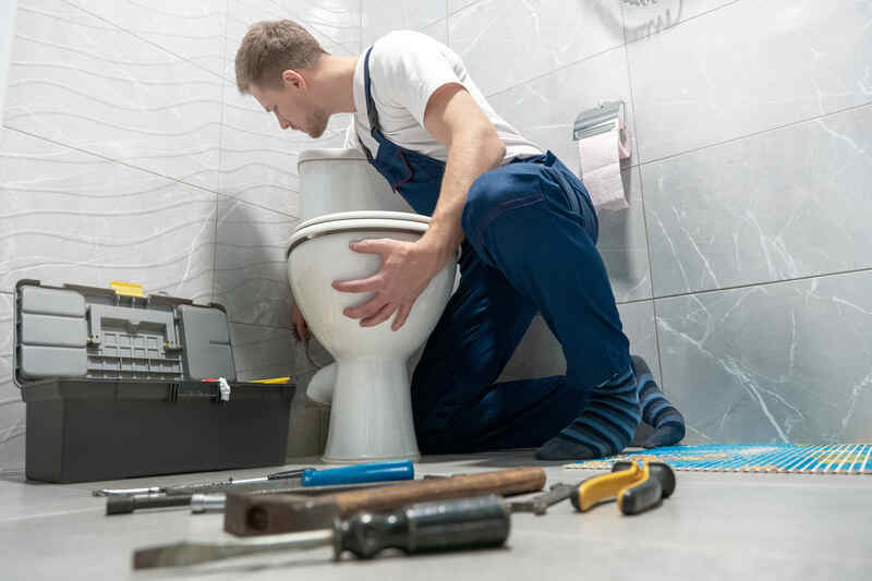man plumber in uniform installing toilet bowl using instrument kit