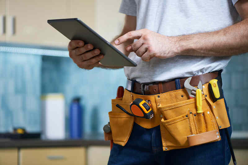 plumber wearing a tool belt with various tools using digital tablet