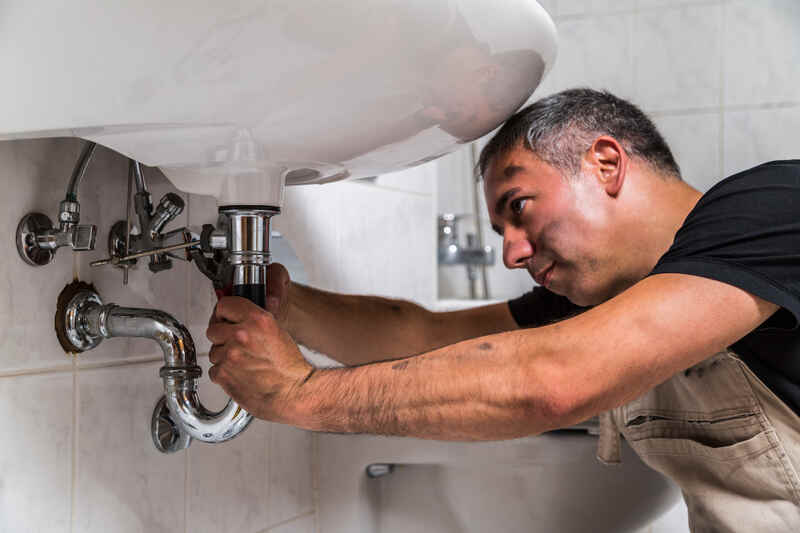 Professional male plumber repairs faucet in bathroom