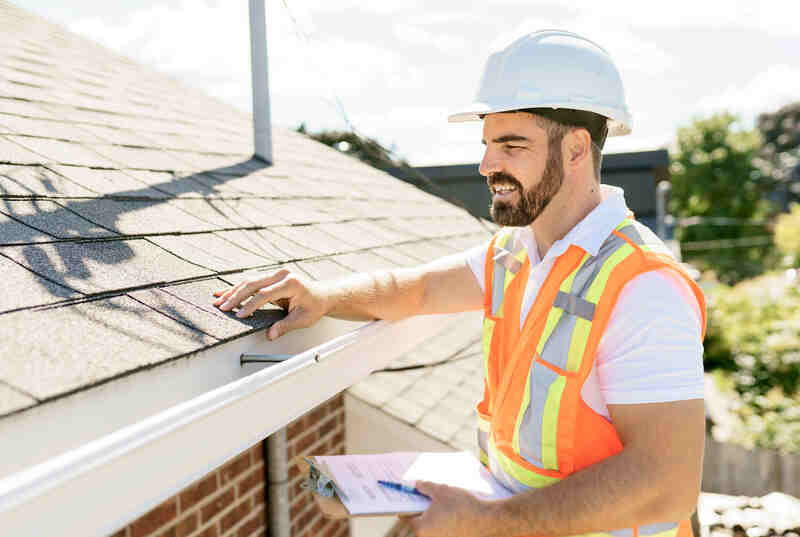 A man in a hard hat, holding a clipboard, standing on the steps of an old rundown house