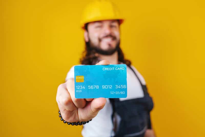 Bearded young man contractor worker with credit card on yellow background