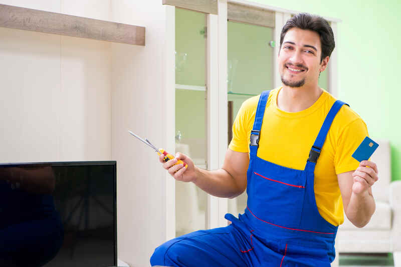 Male professional serviceman repairing tv at home holding credit card