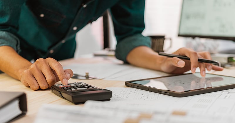 Close up of contractor working on pricing plan with tablet and calculator