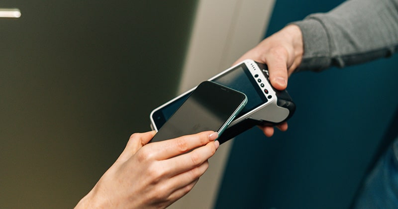 Close up of customer's hand using smartphone to tap card reader for payment
