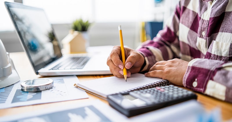 Close up of contractor hands holding pencil with calculator and laptop open