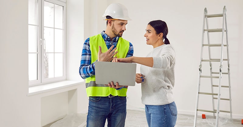 Contractor and client discussing work on laptop during home renovation