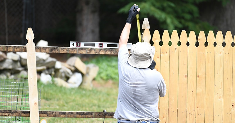 Contractor using measuring tape and level to install wooden fence