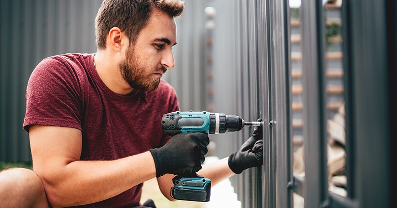 Fencing contractor using cordless electrical screwdriver on metal fence