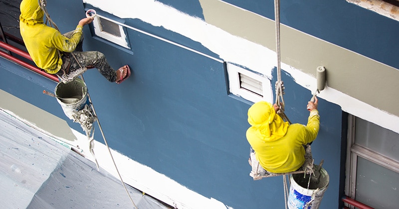 Two painters hanging via ropes, painting on building