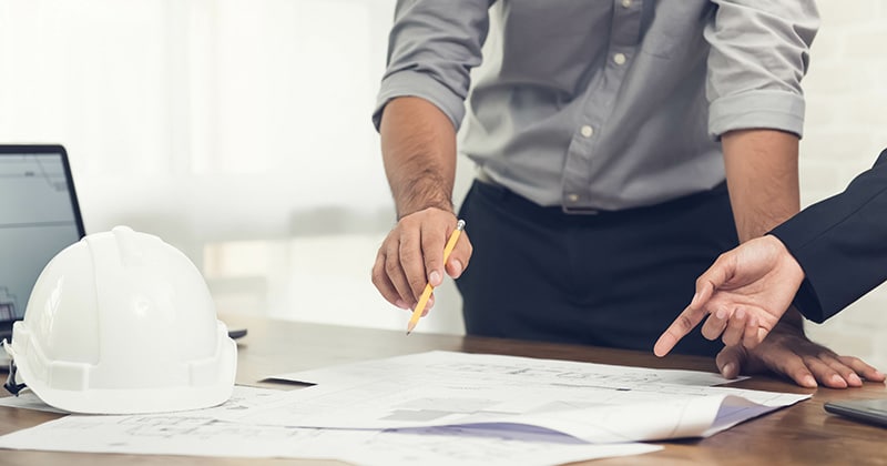 Construction pros discussing project with plans open on table
