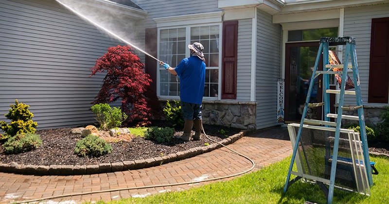 Contractor using a power washer to clean windows and front of home