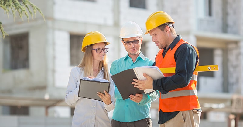 Three building professionals discussing construction estimate outdoors in front of building