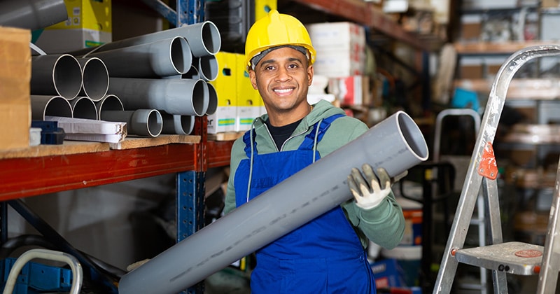 Plumber in protective helmet and overalls selects plastic pipes at hardware store