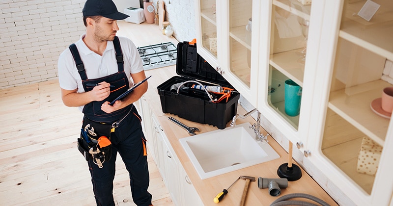 Plumber stands at kitchen sink with tablet in hand