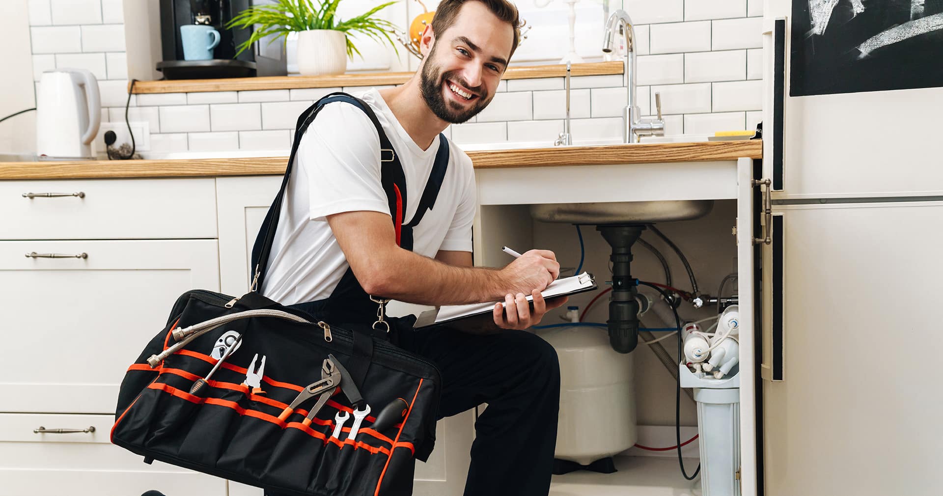 Plumber with equipment and clipboard working in kitchen
