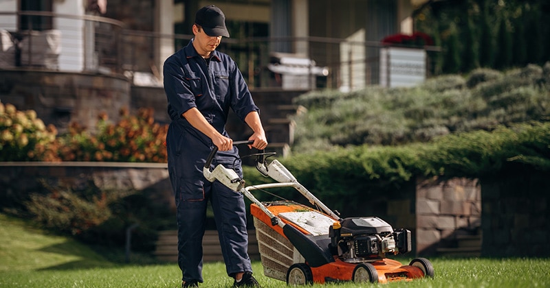 Professional lawn care worker using push lawn mower to cut grass