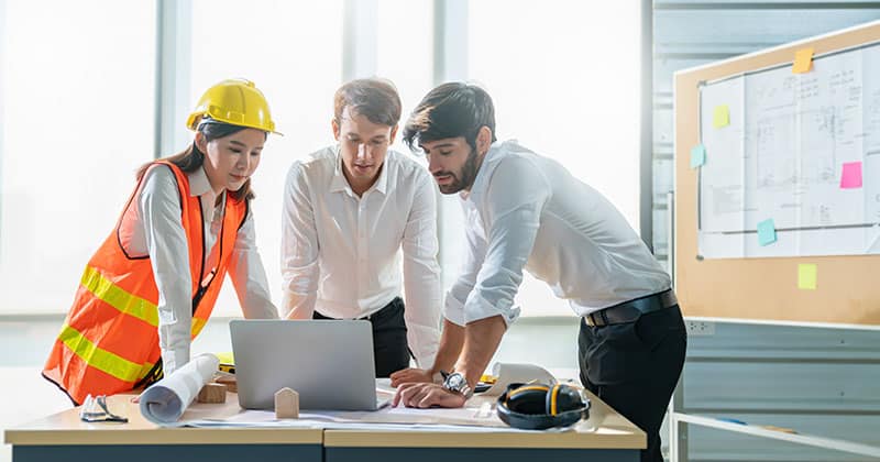 Construction estimator works with engineers in office, in front of open laptop