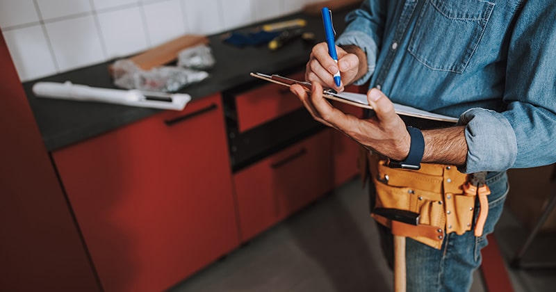 Handyman writing on clipboard in kitchen