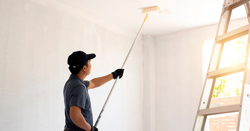 Painter uses roller to paint ceiling in home