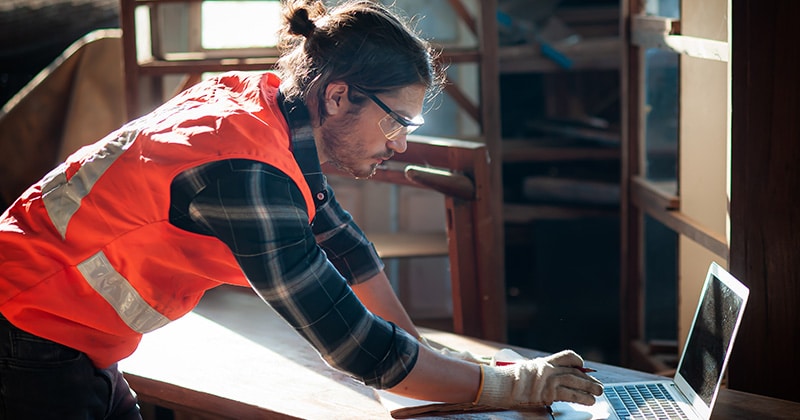 Carpenter in shop works on laptop