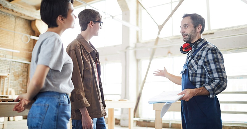 Carpenter in workshop speaks with two clients