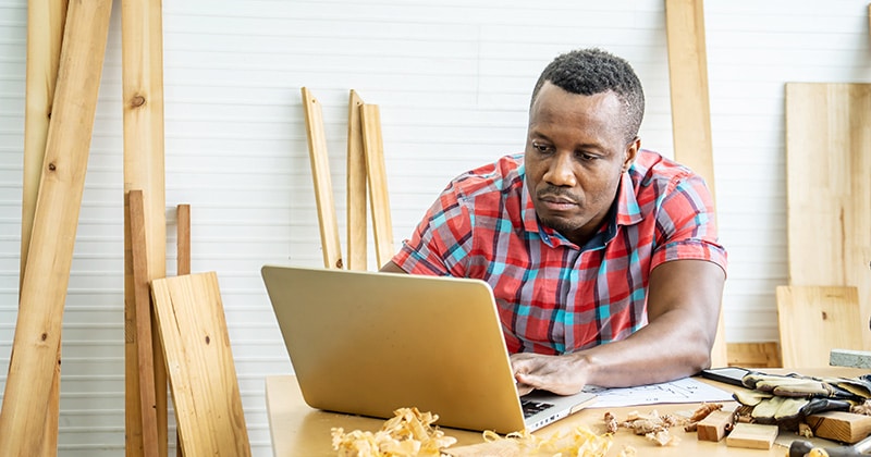 Carpenter sitting at table working on computer in workshop