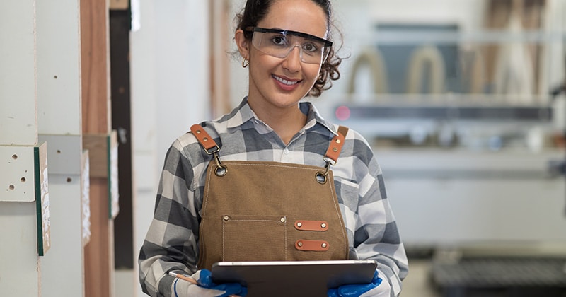 Carpenter wearing safety goggles holding tablet and pencil
