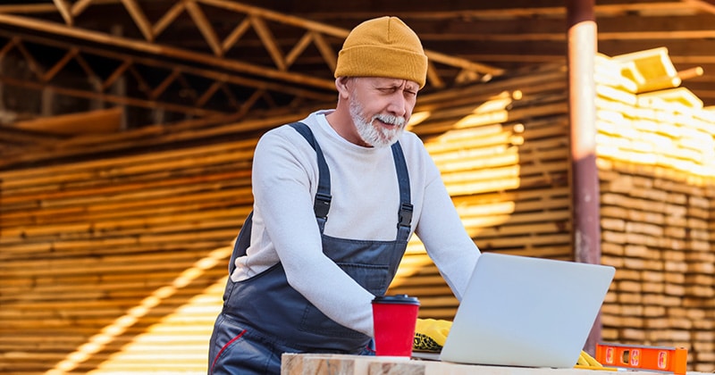 Carpenter with laptop and coffee in front of supplies