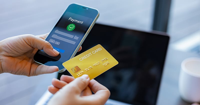 Closeup of card tapping on phone to make mobile payment with laptop in background