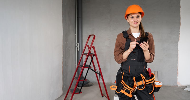 Contractor in helmet at construction site with smartphone