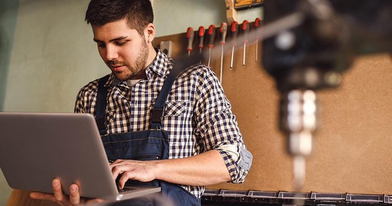 Contractor in studio on laptop with tools in background