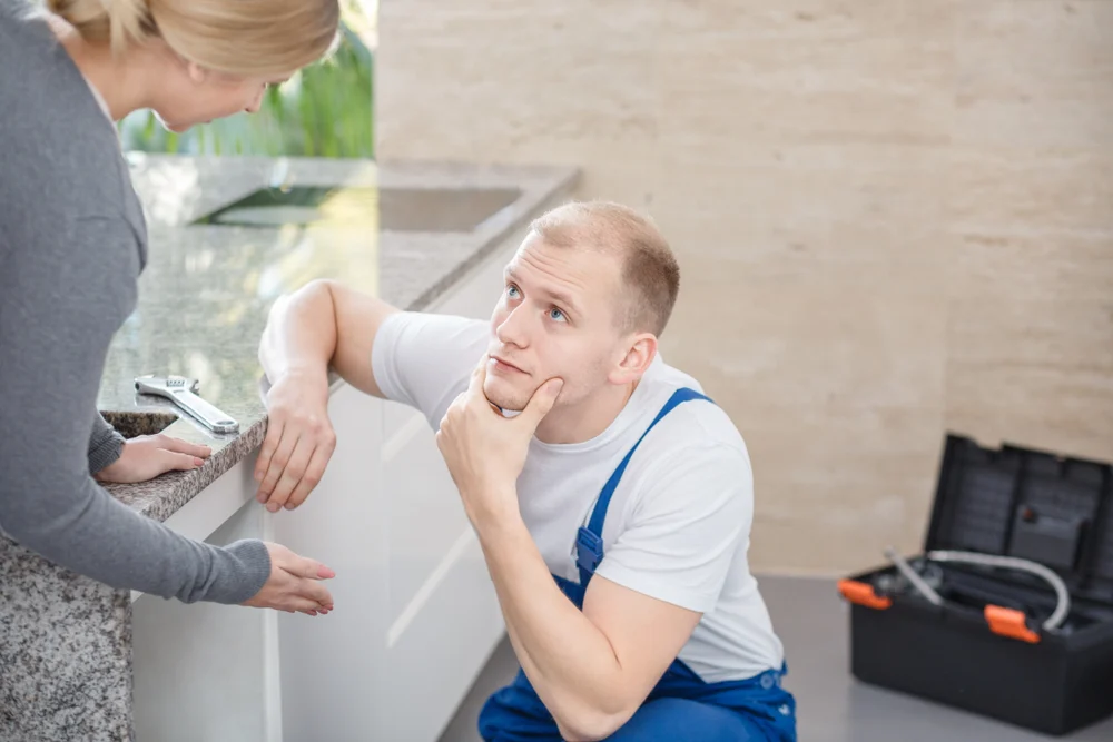 Contractor kneeling looks up at client who is describing problem