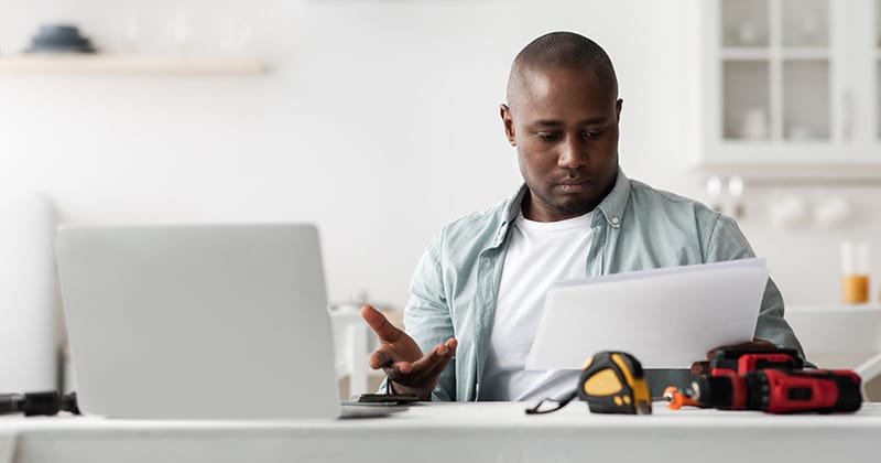 Contractor reading documents with laptop open in front
