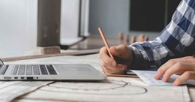 Contractor working on laptop and on paper in home office