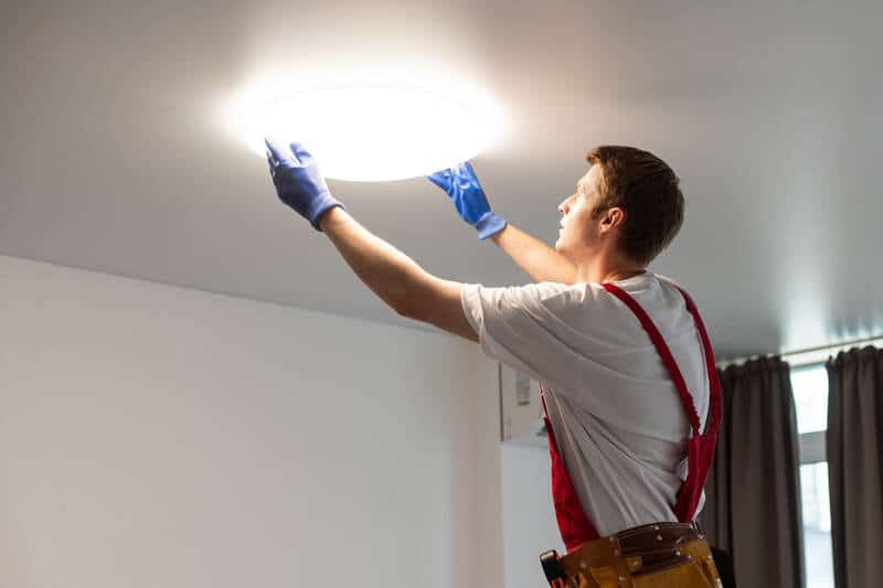 Electrical contractor installing lamp on stretch ceiling indoors