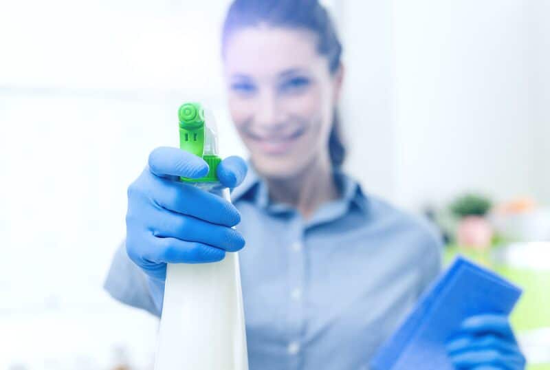 Female cleaner using a spray detergent looking at the camera