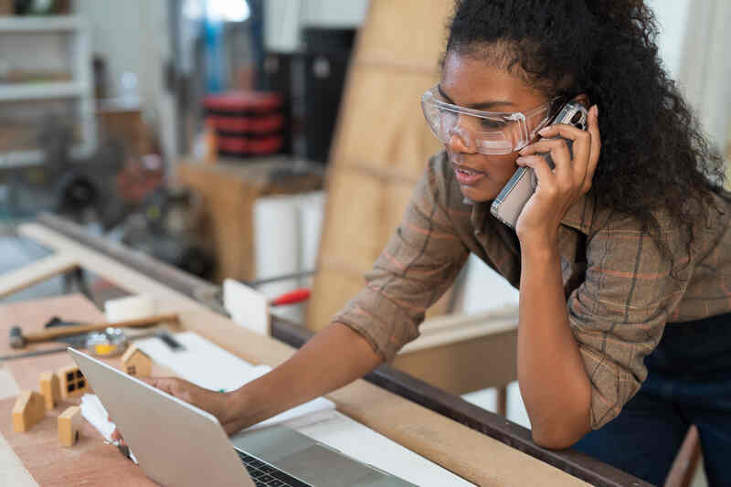 Female contractor using smart phone and working with laptop 