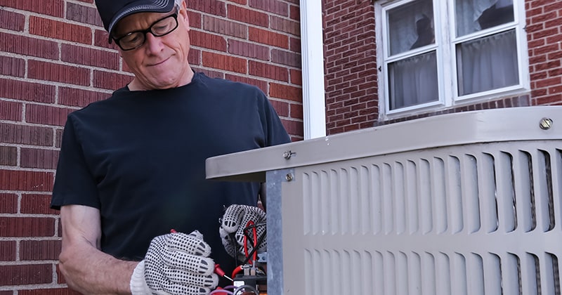 HVAC technician repairing AC unit outside home