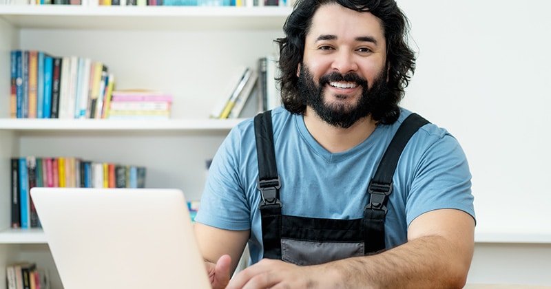 Home pro smiles at camera in front of open laptop in home office