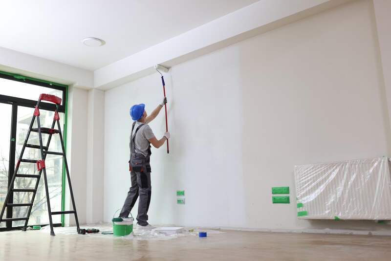 Male painter paints wall with roller brush