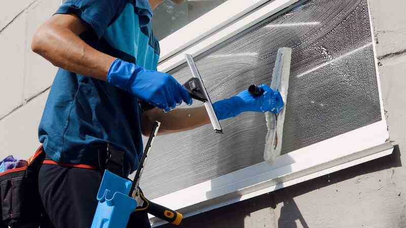Male professional cleaning service worker in overalls cleans the windows with special equipment